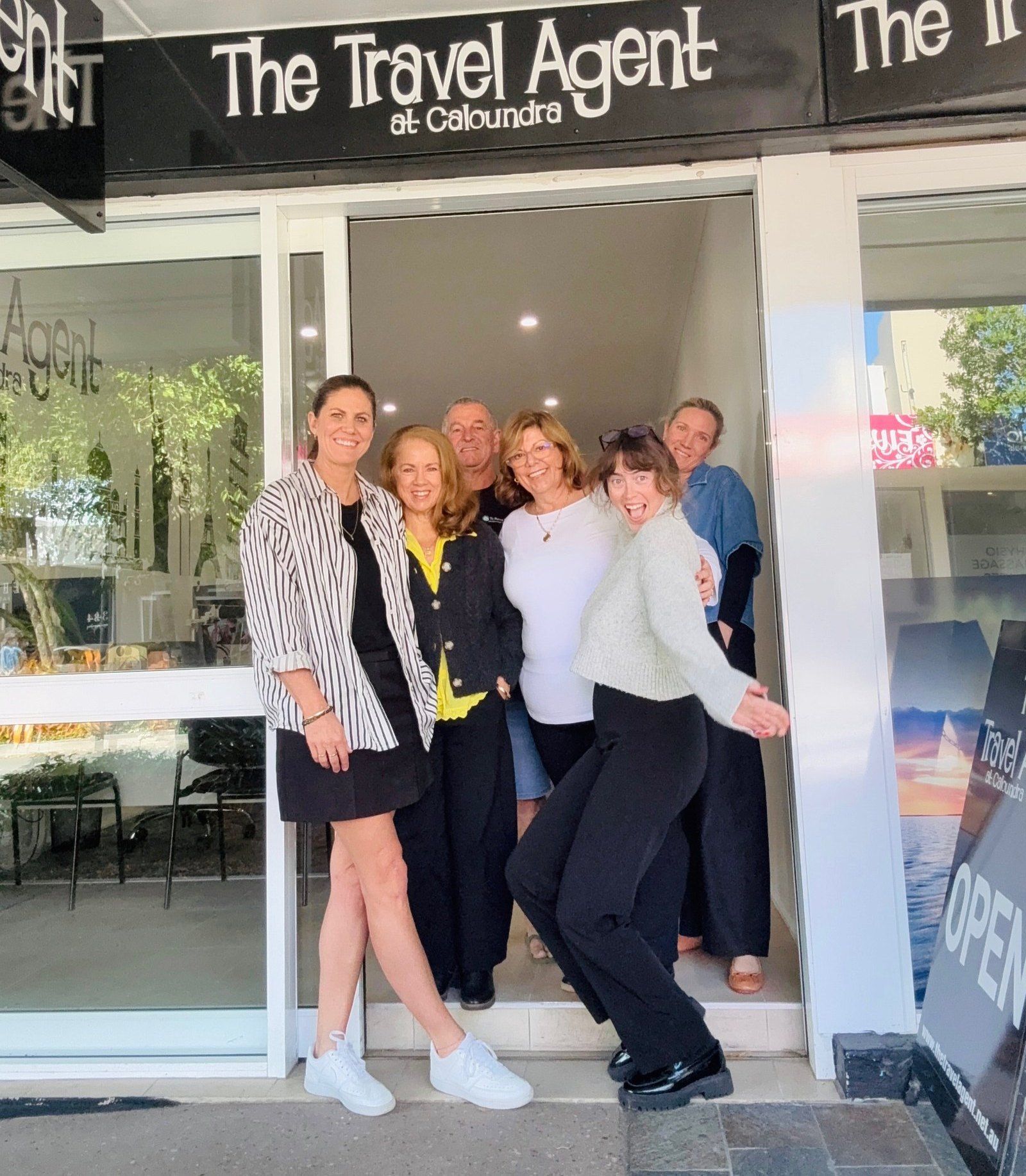 The team standing together in the doorway of the new shop, under The Travel Agent sign